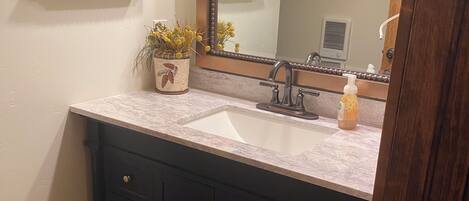 A bathroom with a marble sink, dark wooden cabinets, and decorative items on a shelf.