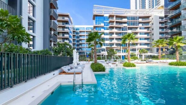 Un hotel moderno con piscina, varios balcones y abundante vegetación.