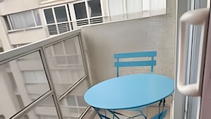 A small balcony with a blue table and matching chairs, a glass railing, and a textured wall. - Apartamento Familiar en Santiago (Santiago)