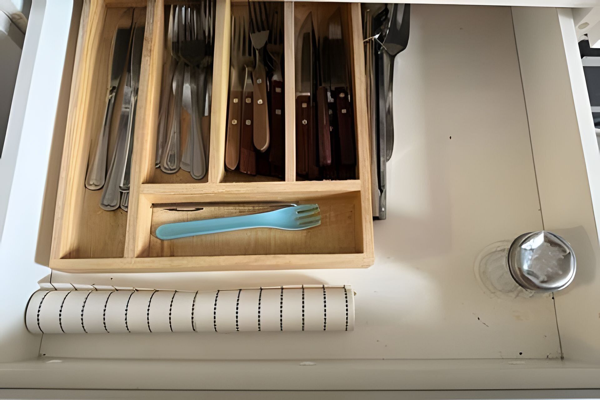 A drawer with a wooden utensil organizer containing various kitchen tools.