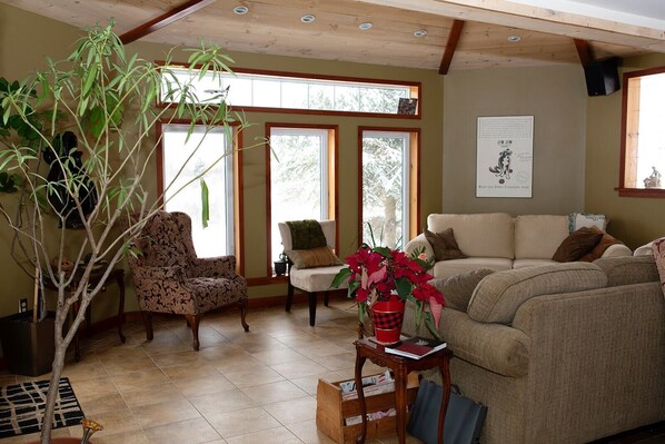 A cozy living room with a large window, a sofa, a chair, and a potted plant. - Charming Rustic Farmhouse in NS Wine & Ski Country, The Gaspereau Valley! (Wolfville)