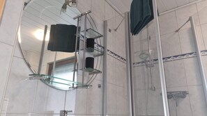 A bathroom with a glass shower enclosure, a glass shelf with toiletries, and a large mirror.