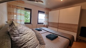 Een slaapkamer met twee bedden, een bank en een groot raam.