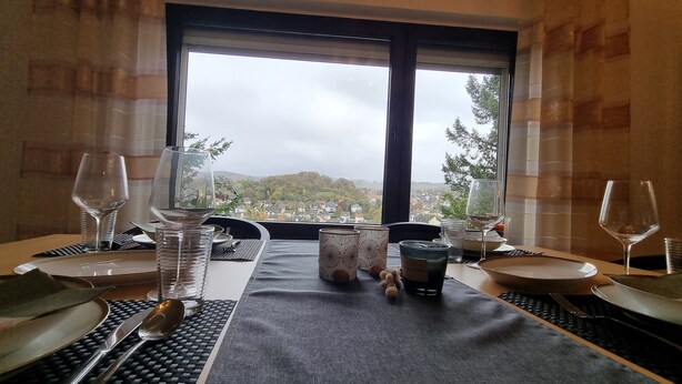 Een eettafel gedekt met borden, bestek, glazen en een kaars, met een mooi uitzicht door het raam.
