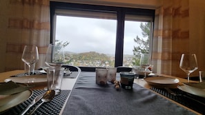 A dining table set with plates, cutlery, glasses, and a candle, with a scenic view through a window. - Vacation Apartment II with a Panoramic View in Arnsberg's Old Town (Arnsberg)