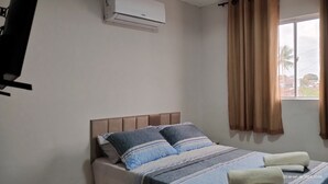 Un dormitorio con cama, ventana con cortinas, aire acondicionado y televisor de pared.