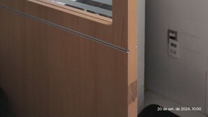 Una habitación con un armario de madera, una estantería blanca con un jarrón y una ventana con persianas.