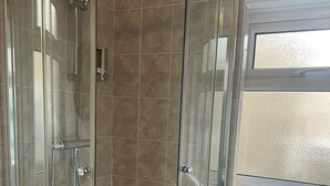 A glass-enclosed shower stall with a curved design, tiled walls, and a window above. - OYO The Board Inn (Hawes)