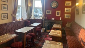 A cozy pub with wooden tables and red upholstered benches, a fireplace, and framed pictures on the walls. - OYO The Board Inn (Hawes)