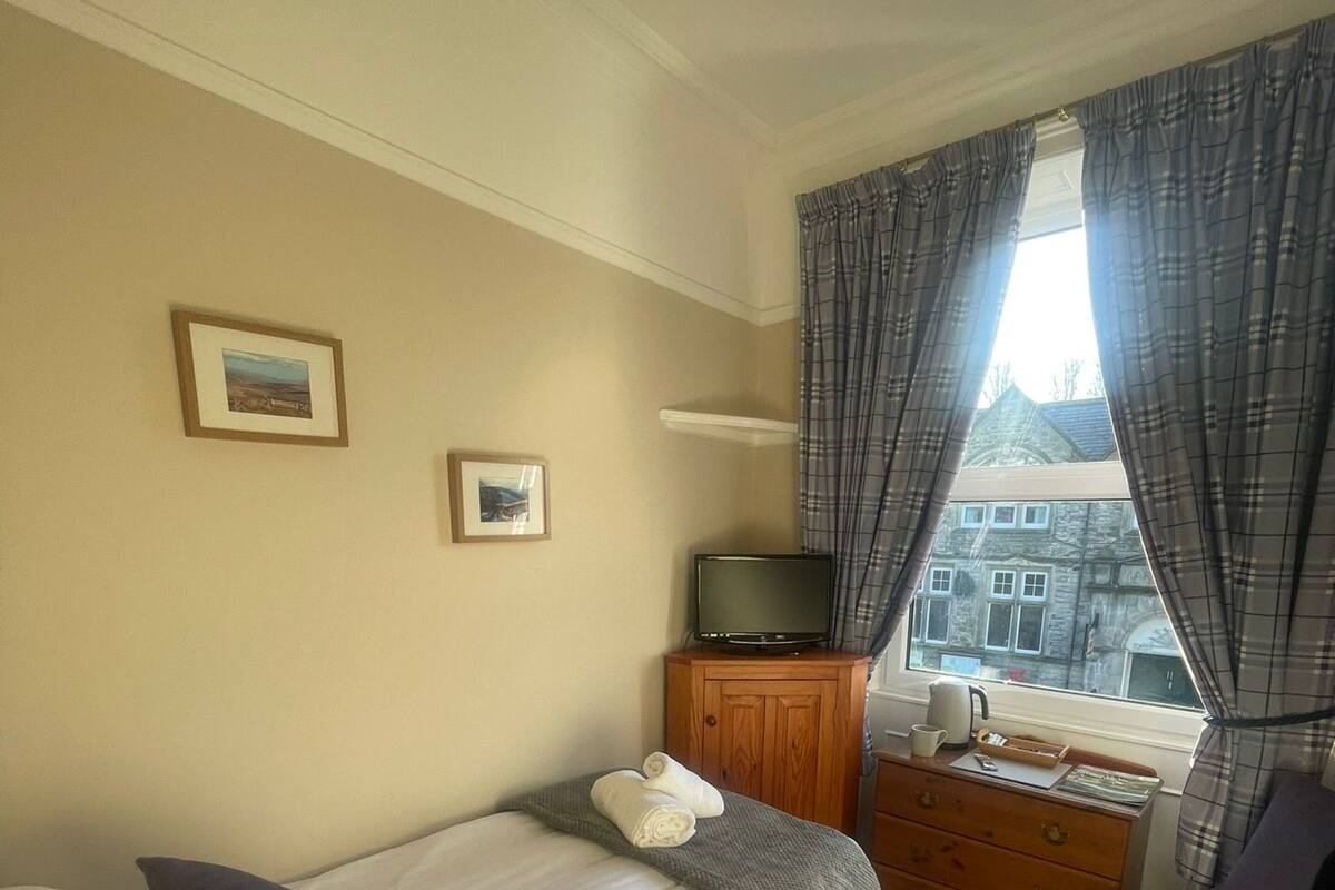 Une chambre d’hôtel avec un lit, une télévision, une commode et une fenêtre avec des rideaux.
