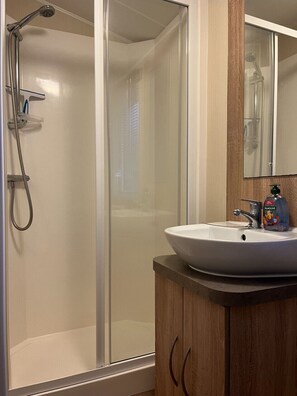 Bathroom features a glass shower enclosure, handheld showerhead, and wall-mounted faucet, along with a vanity with a sink and mirror.