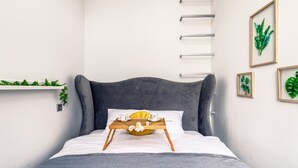 A bed with a grey upholstered headboard, a white pillow, and a tray with a yellow bowl and white flowers. There are framed green leaves on the wall. - Środmieście Apt - Top Location, Tram&Park nearby - by Rentujemy (Wroclaw)