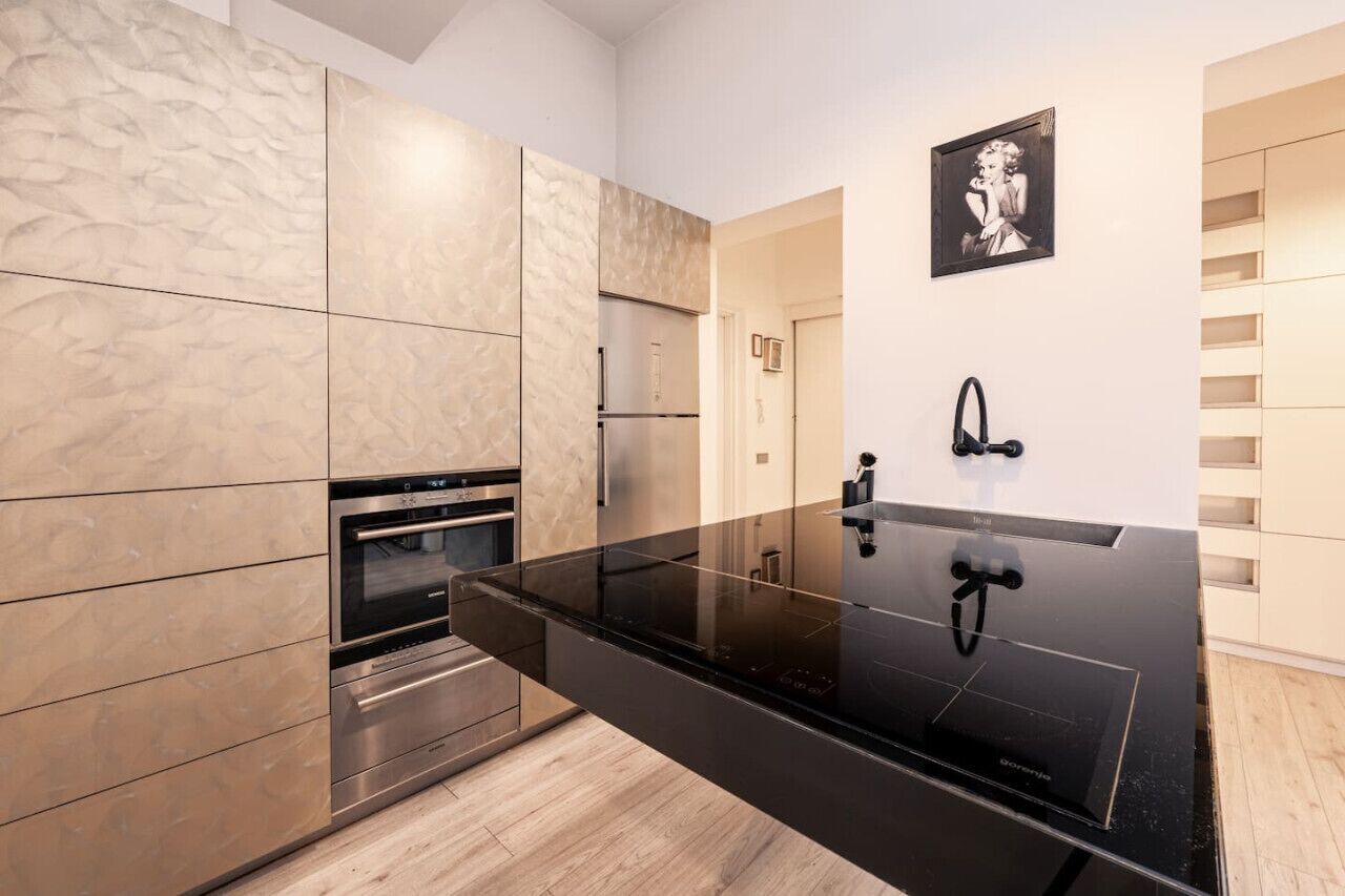 A modern kitchen with a black countertop, stainless steel appliances, and a marble backsplash.