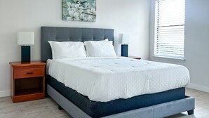 Une chambre moderne avec un lit recouvert d’un tissu gris, une literie blanche et un mur d’accent bleu.
