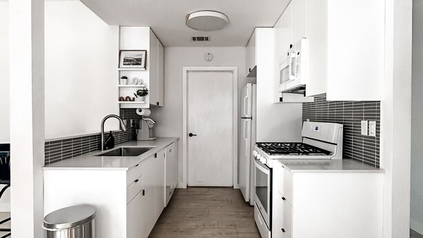 Une cuisine moderne avec des meubles blancs, une poubelle en acier inoxydable, un four à micro-ondes et une cuisinière.