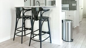 Une cuisine moderne avec des meubles blancs, un évier en acier inoxydable et une poubelle.