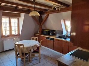 A kitchen with a dining table, chairs, a coffee maker, and a window with curtains.