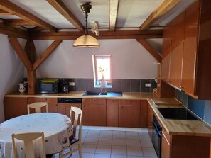 A kitchen with wooden beams, a window, a sink, and a dining table with chairs.
