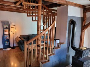 A wooden spiral staircase in a room with a dark-colored sofa, a wall-mounted heater, and a black stove.