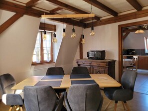 Ein Essbereich mit Holztisch und -stühlen, im Hintergrund eine Küche und eine schräge Decke mit sichtbaren Balken.