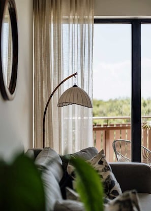 A living room with a sofa, a floor lamp, and a view of a balcony.