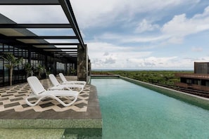 Una piscina infinita en la azotea con sillones blancos, vista despejada al océano y diseño arquitectónico moderno.