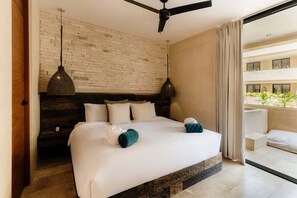 Una camera d'albergo con un muro in mattoni, un letto con lenzuola bianche, due lampade a sospensione e una ventola a soffitto.