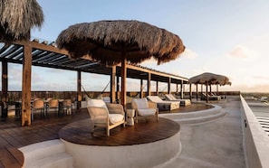 A wooden deck with thatched umbrellas, lounge chairs, and a pool area.