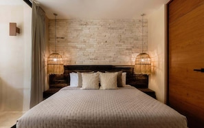 A bedroom with a brick-patterned headboard, a large bed with a textured duvet, two bedside lamps, and a wooden door.