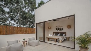 A modern bedroom with a large glass wall, a bed with a wooden headboard, a small round table, and a potted plant. - Maki Mystical Tulum Villa Beach Club Access (Tulum)