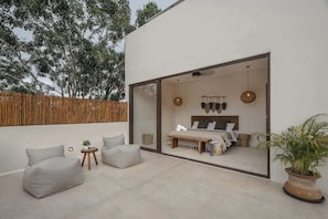 Un dormitorio moderno con un amplio ventanal, una cama con cabecera de madera, una mesita redonda y una planta en maceta.