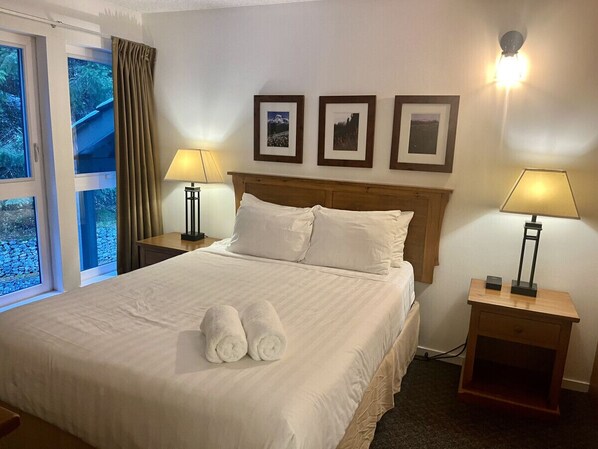 A hotel room with a large bed, two bedside tables with lamps, a wooden headboard, and three framed pictures on the wall.
