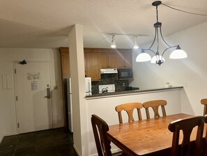 A compact kitchen with wooden cabinets, a microwave, and a dining area with a wooden table and chairs.