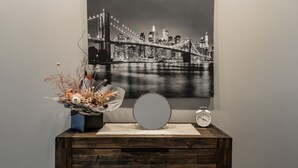 A framed black and white cityscape with a bridge, a decorative vase with dried flowers, a round mirror, and a vintage alarm clock on a wooden dresser. - Modern studio w/t wifi & parking (Kingston)