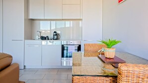 A modern kitchen with white cabinets, stainless steel appliances, and a dining area with wicker furniture and a potted plant. - Modern studio w/t wifi & parking (Kingston)