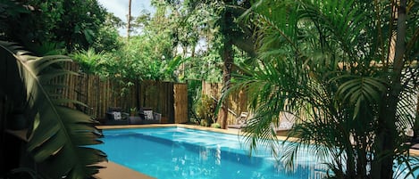 Una piscina rodeada de abundante vegetación y una valla de bambú.
