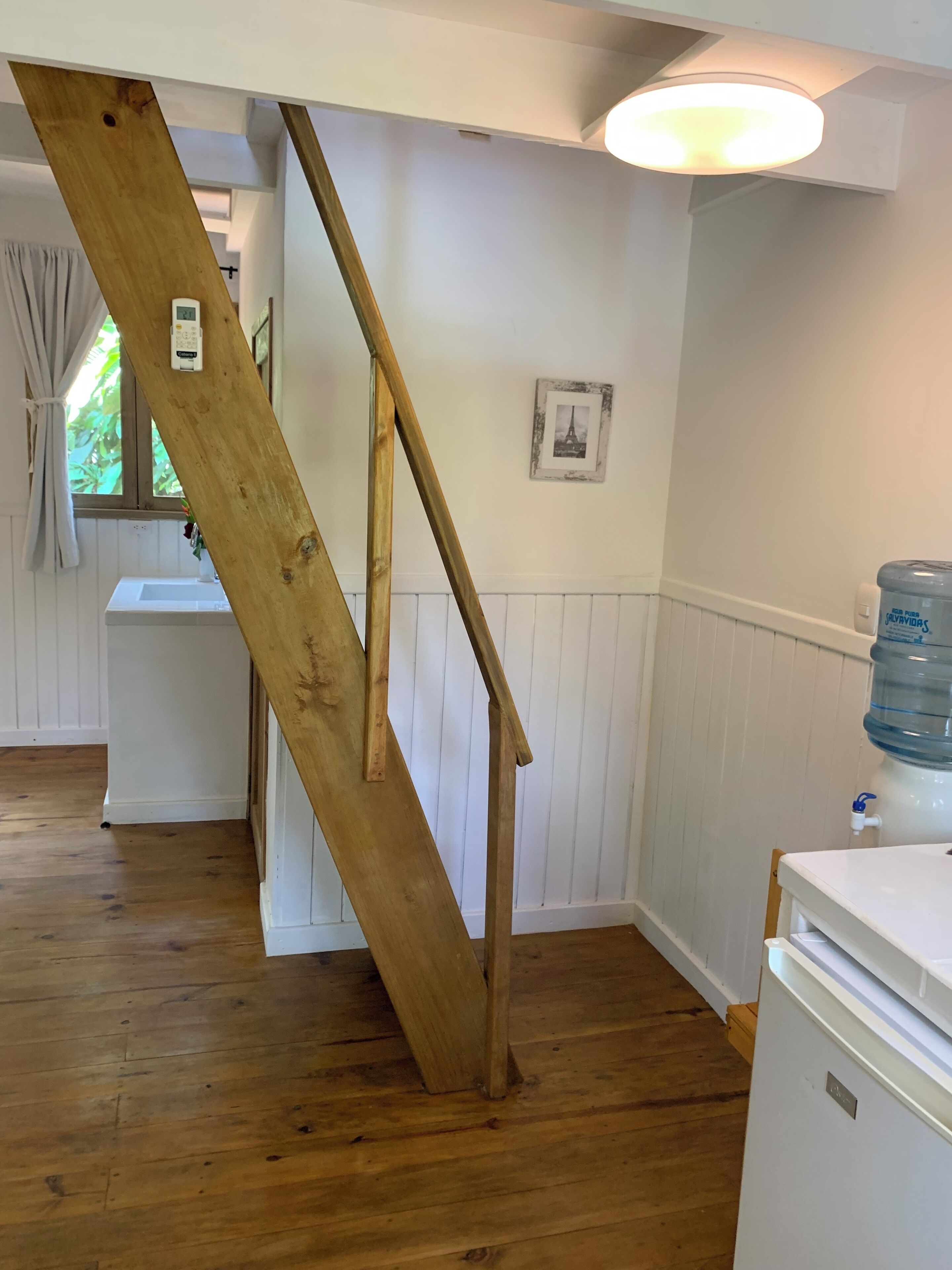 A room with a wooden staircase, a white sink, a water dispenser, and a framed picture on the wall.