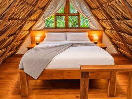 Una cama en una habitación con techo y paredes de madera, una ventana con cortinas y dos lámparas de noche.