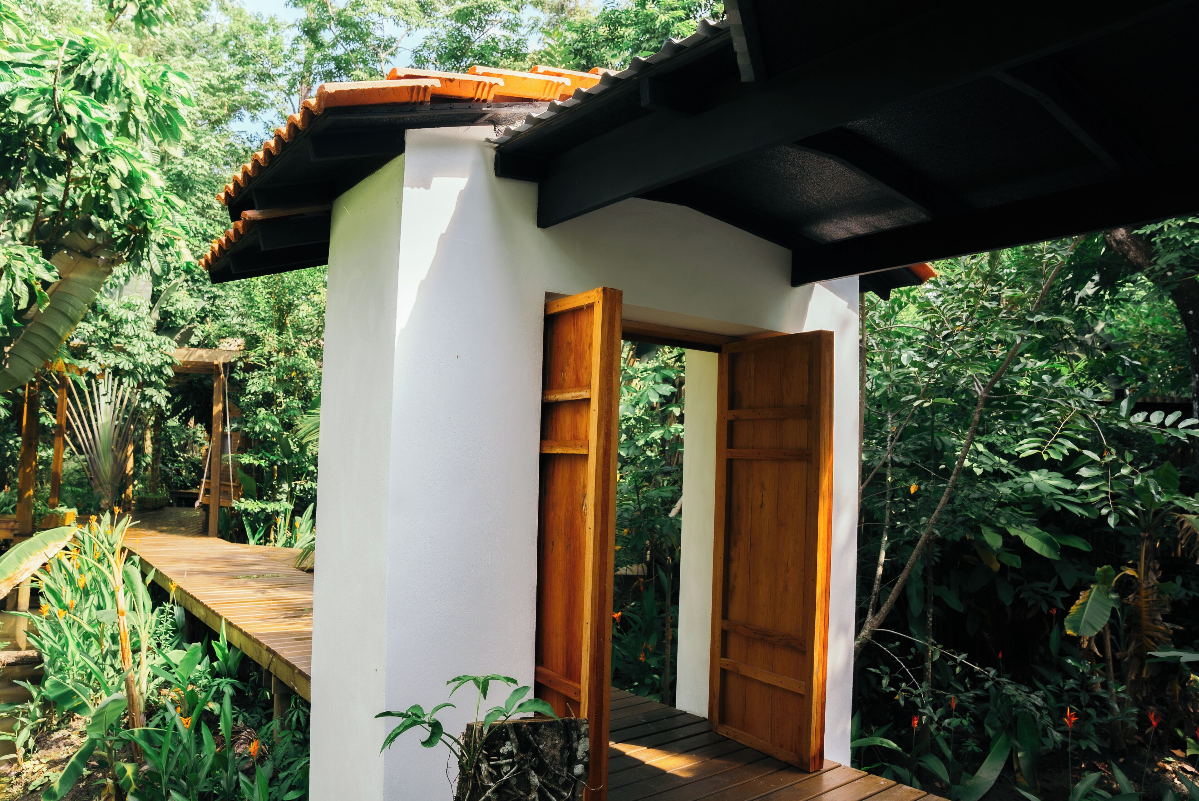 A wooden structure with a white wall and a wooden door, surrounded by lush greenery.