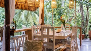 An outdoor dining area with wooden tables and chairs, surrounded by lush greenery. - Boatique Hotel and Marina (Livingston)