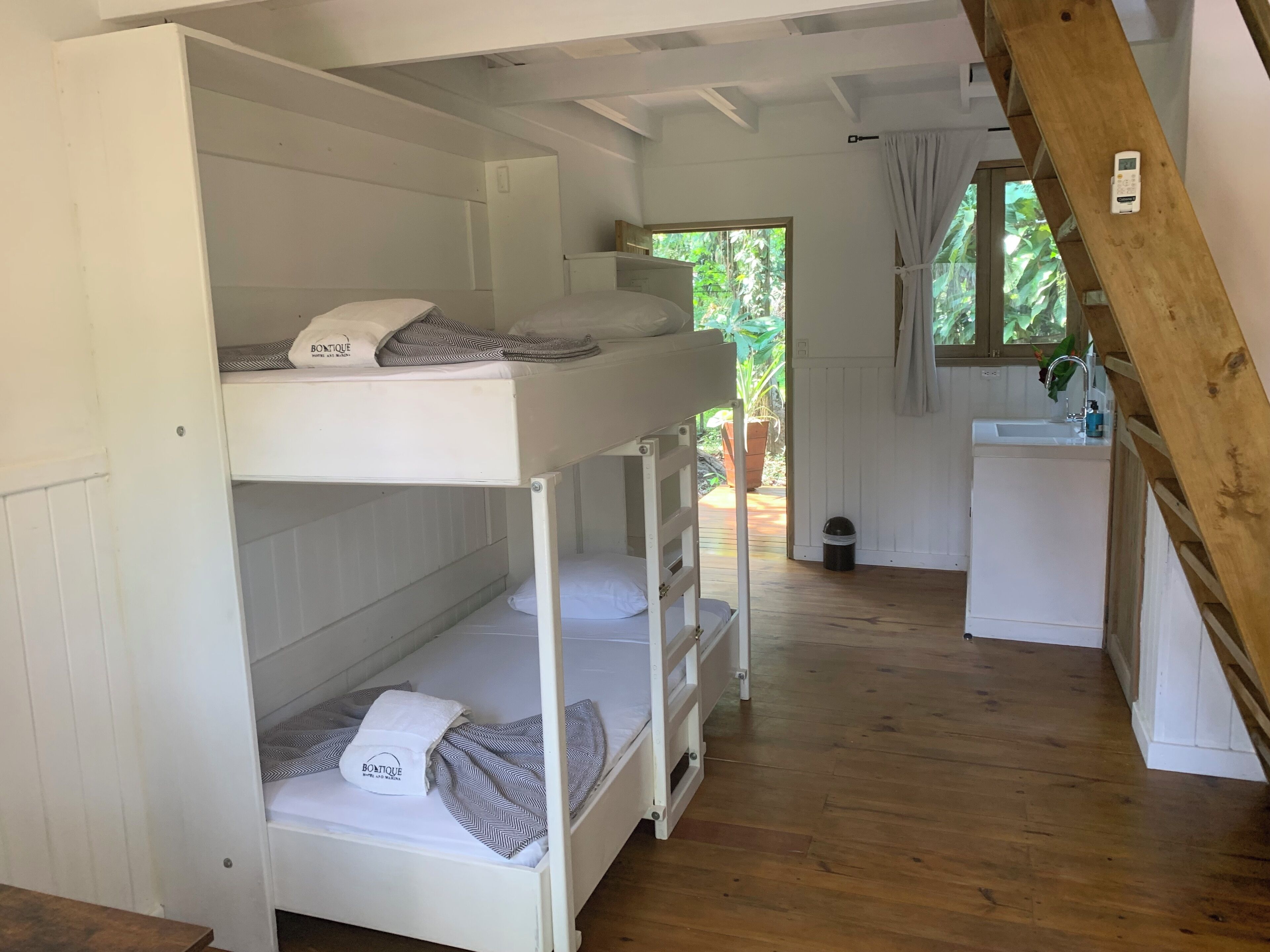 A bunk bed room with a wooden ceiling, a small kitchenette, and a window with curtains.