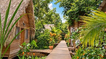 Un sendero de madera conduce a cabañas con techo de paja, rodeadas de exuberante follaje y plantas tropicales.