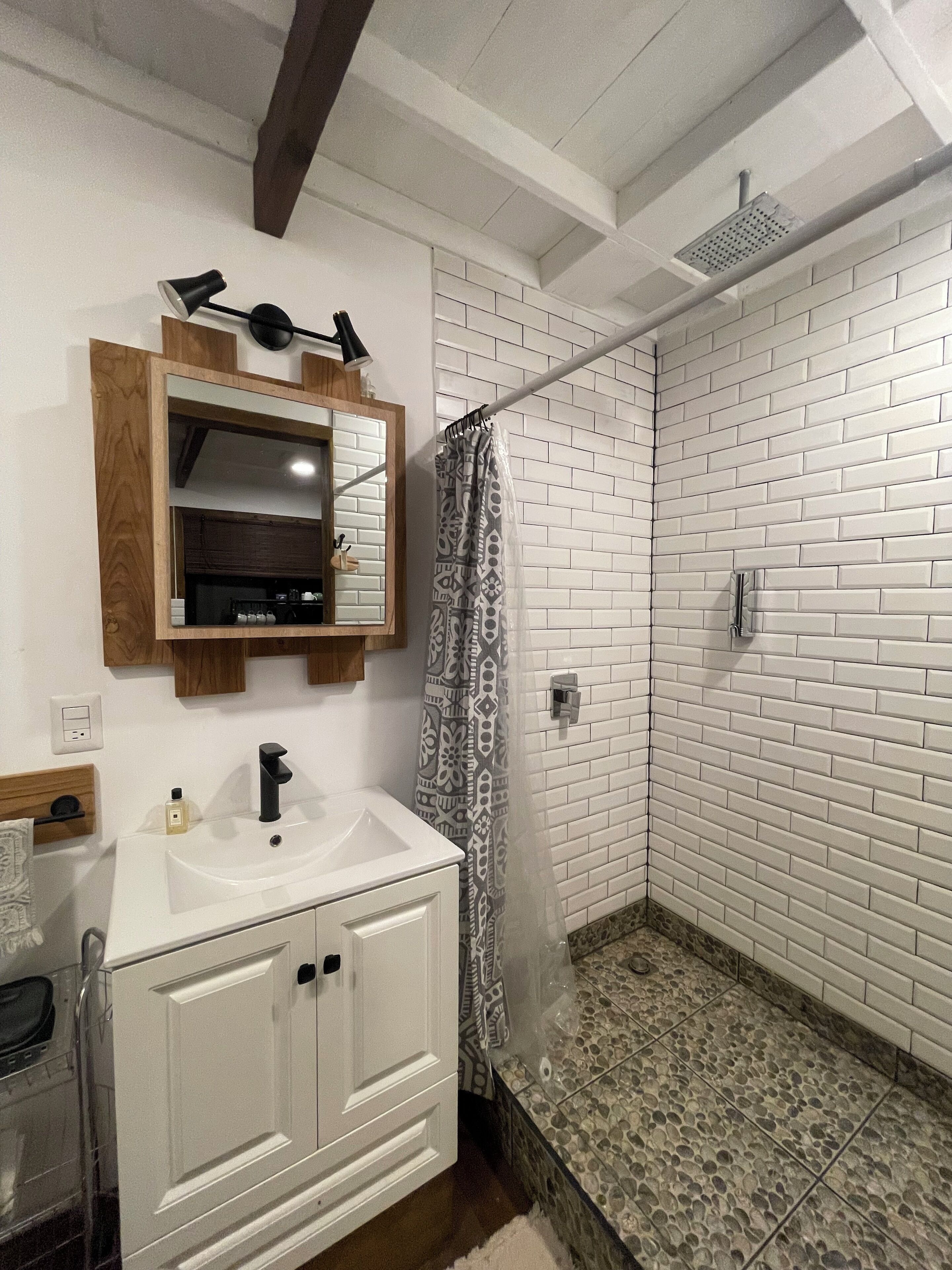 Ein Badezimmer mit weißem Waschbecken, Holz-Badmöbeln, Spiegel und einem duschvorhang mit Muster.