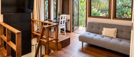 A modern living room with a sofa, a TV, a dining area with a table and chairs, and a large window with a view of greenery.