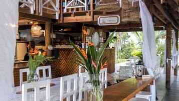 A wooden bar area with white chairs and stools, hanging wicker baskets, and a sign reading "BOUTIQUE".