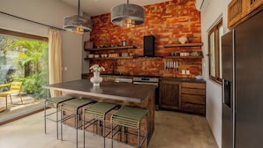 A modern kitchen with a large island, bar stools, hanging lights, and a brick backsplash. - Casa Wabi in Sayulita (Sayulita)