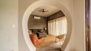 A room with a curved ceiling, a ceiling fan, a sofa, a chair, and a window with sheer curtains. - Casa Wabi in Sayulita (Sayulita)