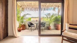 A room with a sliding glass door leading to a balcony with potted plants and a view of the city. - Casa Wabi in Sayulita (Sayulita)