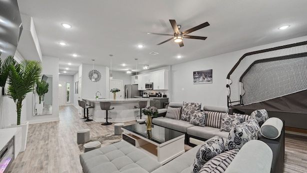 A modern living room with a sofa, coffee table, and a dining area with bar stools. - Chic Modern Getaway: Indoor Basketball, Huge TVs, & Smart Living (Houston)