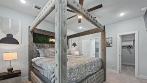 A four-poster canopy bed with a tufted headboard, a nightstand with a lamp, and a wall-mounted artwork. - Chic Modern Getaway: Indoor Basketball, Huge TVs, & Smart Living (Houston)
